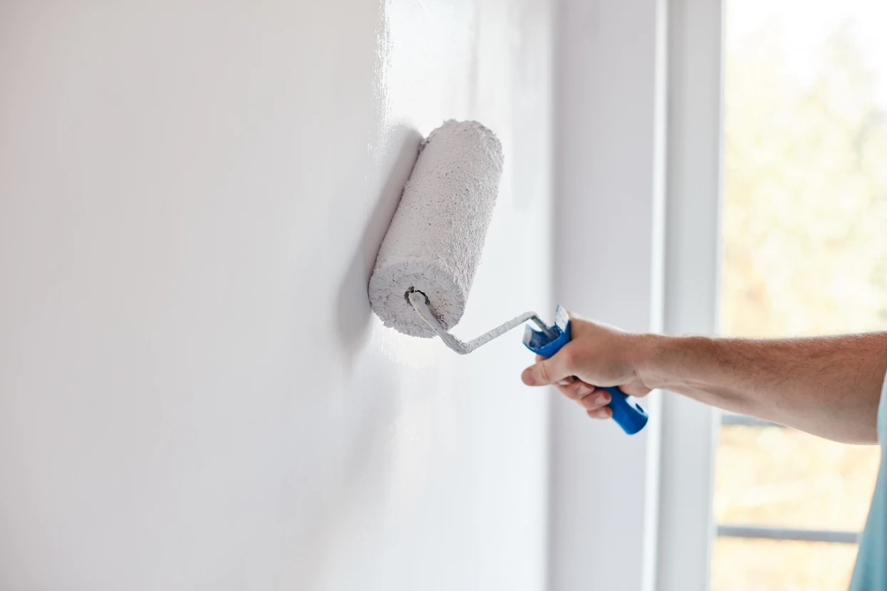Intérieur résidentiel avec personne appliquant de la peinture blanche sur un mur à l'aide d'un rouleau à peinture