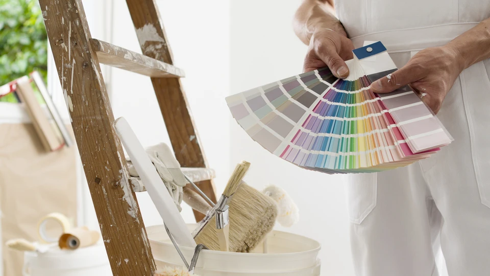 Peintre en bâtiment tenant un nuancier colorimétrique en éventail dans un intérieur en rénovation