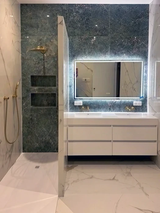 Salle de bain luxueuse avec douche italienne carrelée en marbre vert foncé veiné, robinetterie dorée brossé, niche murale encastrée